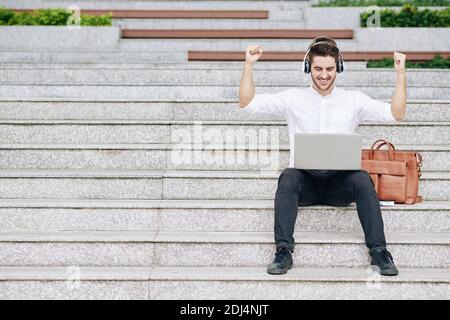 Excited young businessman raising arms to celebrate finishing big project he was working on Stock Photo