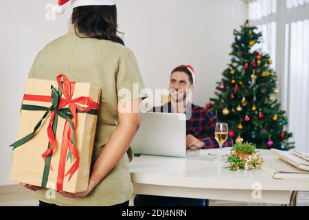Businesswoman hiding big decorated Christmas present for colleague behind her back Stock Photo