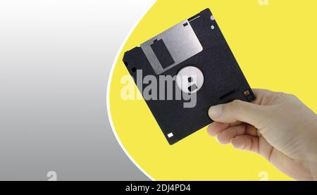 Floppy disk in human hand isolated on gray and yellow background Stock Photo