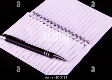 Pen and opened A5 notepad with white lined pages and spiral boound with a black background Stock Photo