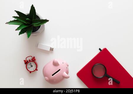 Freelance office workplace work concept. Red notebook, nature plant, alarm clock and pencils on a white minimalistic background with copy space. Minimal work space Stock Photo