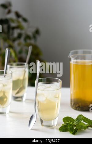 Cold refreshing green tea with ice and mint, tea jug and glasses on white wooden background Stock Photo