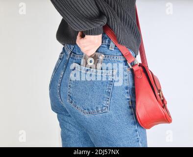 A girl in a mimes fit jeans, a sweater and with a red bag on the edge pulls out a retro audio cassette from her pocket on a white background. Side vie Stock Photo
