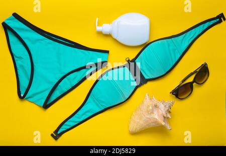 Accessories for the resort on the beach on a yellow background. Swimsuit, sunblock, sunglasses, shell. Top view. Stock Photo