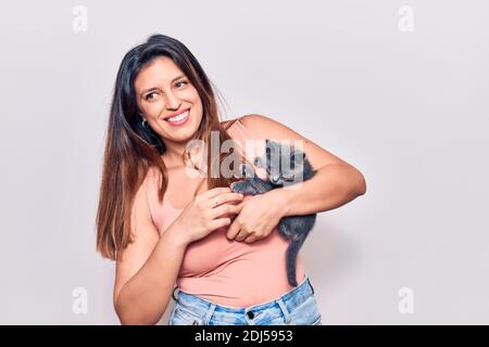 Young beautiful latin woman smilling happy. Standing with smile on face holding adorable cat over isolated white backgroun Stock Photo