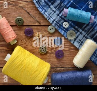 Colored threads, buttons, a needle on a wooden table. Objects for sewing. Top view. Stock Photo