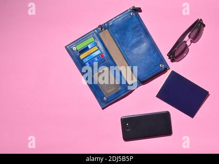Accessories for traveling on a pink background: a purse with credit cards, a smartphone, a passport, sunglasses. Top view. Stock Photo