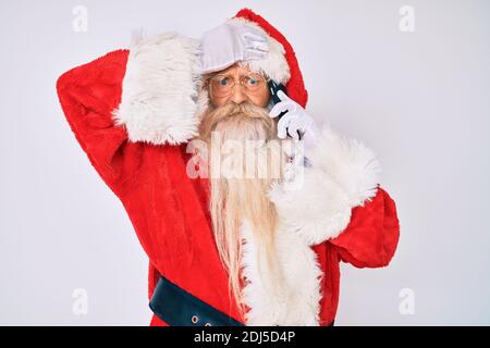 Old senior man wearing santa claus costume speaking on the phone stressed and frustrated with hand on head, surprised and angry face Stock Photo