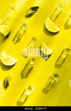 Fresh mint leaf and ice cubes with droplets and lime on illuminating yellow background. Summer background Stock Photo