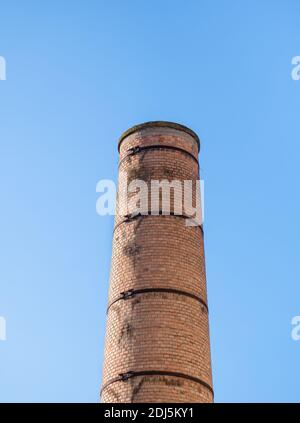 Old factory chimney made of red bricks against blue sky. Stock Photo