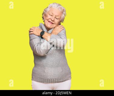 Senior grey-haired woman wearing casual winter sweater hugging oneself happy and positive, smiling confident. self love and self care Stock Photo