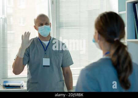 Mature male medical laboratory worker waving hand to his young female assistant while greeting her in the beginning of working day Stock Photo
