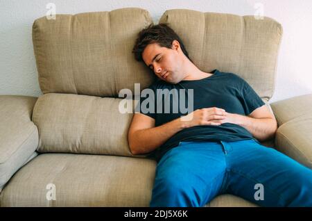 A young redhead guy in a black T-shirt sleeping on a cream sofa Stock Photo