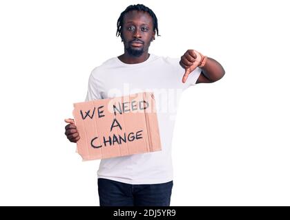 Young african american man with braids holding we need a change banner with angry face, negative sign showing dislike with thumbs down, rejection conc Stock Photo