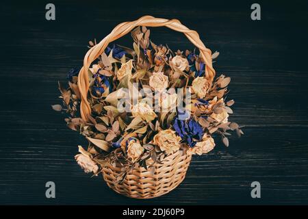 Vintage basket with yellow and blue roses. Dried dead flowers on a black wooden background Stock Photo