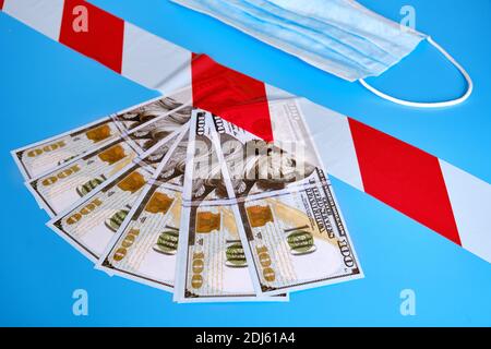 Money USA dollars, signal tape and protective mask on a blue background. The concept of problems in America financial system due to economic under the Stock Photo
