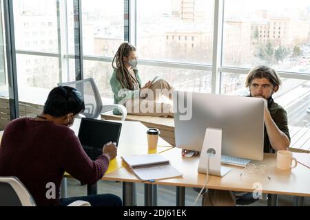 Young businessman looking at computer screen while his male colleague networking in front of laptop and businesswoman using digital tablet Stock Photo
