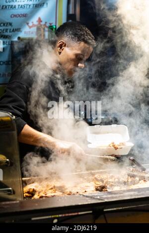 Manchester December 2020. Christmas street markets selling food near Piccadilly Gardens. A man serving curry at a food stall shrouded in steam Stock Photo