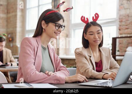 Two young successful intercultural businesswomen in elegant casualwear working over report for forthcoming conference on xmas day in office Stock Photo