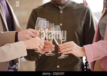 Hands of four young colleagues clinking with flutes of champagne during toast for new business partnership at corporate party in office Stock Photo
