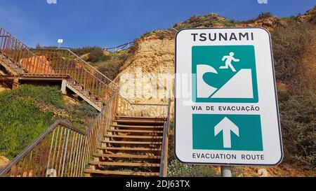 Sign indicating egemergency exit from the beach on the old rusty stairs to the sandy mountain. Stock Photo