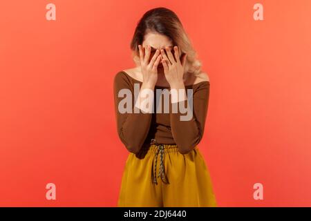 Oh no, it can't be! Portrait of sad young woman standing, who dramatic covered face with her palms, feeling trouble, pain and sorrow. Depressed concep Stock Photo