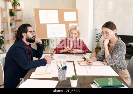 Three intercultural mobile application developers scrolling in smartphones while searching for new ideas for their project in the net Stock Photo