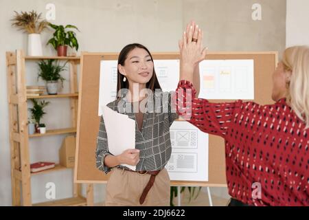Two successful businesswomen in smart casualwear giving one another high five while congratulating on great work over new project Stock Photo