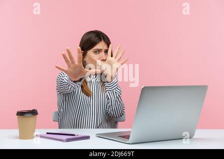 No, I'm scared! Frightened woman with shocked expression raising hands in stop gesture, defending herself, freaked out of troubles working on laptop. Stock Photo