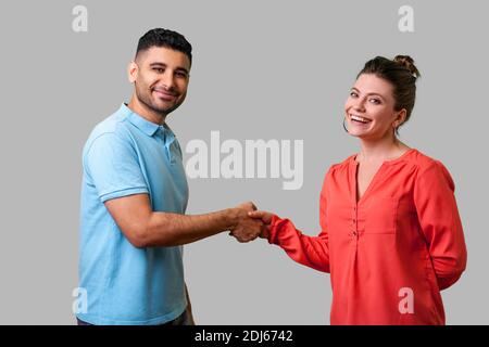 Portrait of lovely young couple in casual wear standing, looking at camera with smile and shaking hands, friendly meeting or acquaintance, greeting. i Stock Photo