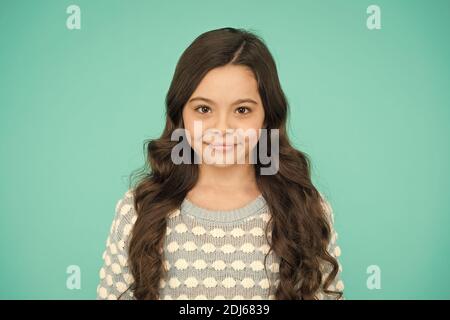 She is really cute. Happy girl child blue background. Small child wear long wavy hair. Little child with cute smile. Beauty salon. Fashion and style. Child care and childhood. Stock Photo