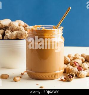 An open jar of peanut butter with a spoon and peanuts in the shell around. Breakfast, food for vegetarians. Copy space. Stock Photo