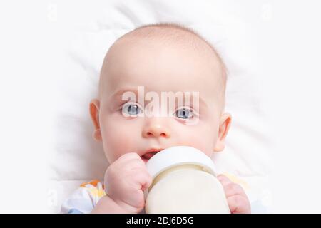 Caucasian baby boy with baby milk bottle on white blanket. Close up. Baby feeding and artificial nutrition concept. Stock Photo