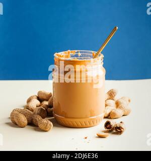 An open jar of peanut butter with a spoon and peanuts in the shell around. Breakfast, food for vegetarians. Copy space. Stock Photo
