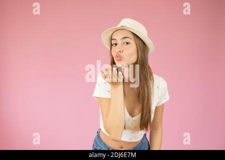 Beautiful young woman with straw hat sending air kiss on pink background Stock Photo