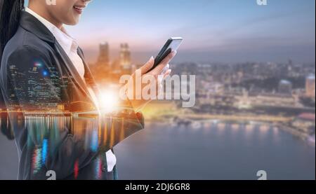 Young businesswoman using mobile phone with modern city buildings background. Future telecommunication technology and internet of things ( IOT Stock Photo