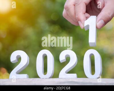 Closeup cement block with number 2021 and hand to Start of New Year plans on nature green background with flare light. Perfect for your invitation car Stock Photo