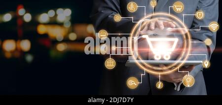 Businessman holding the cart icon Online shopping and payment with a tablet. Shopping cart, Digital marketing, Banking and finance concept. Mixed medi Stock Photo