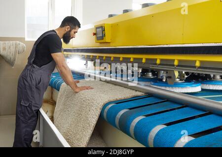 Man operating carpet automatic washing machine in professional laundry service Stock Photo