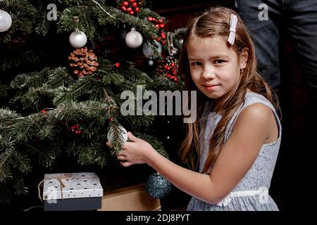 Little girl decorates the Christmas tree in the living room at home.  Cute kid preparing home for xmas celebration. Winter holidays and people concept Stock Photo