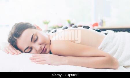 Woman getting hot stone massage treatment by professional beautician therapist in spa salon. Luxury wellness, back stress relief and rejuvenation Stock Photo