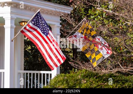 US Flag and Maryland Flag are waving side by side on flag poles in front entrance of a historic house in Rockville, Maryland. There are beautiful shru Stock Photo