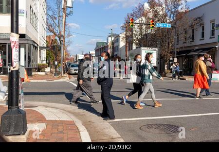 Alexandria, VA, USA 11-28-2020: A group of men and women are crossing the street while an African American female police officer is controlling the tr
