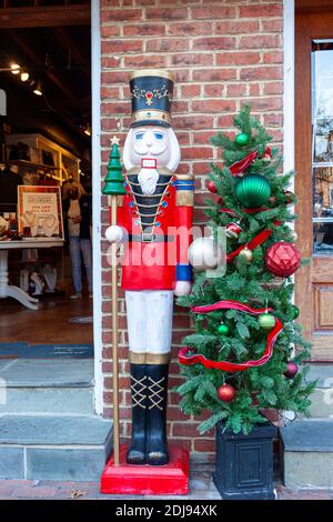 Alexandria, VA, USA 11-28-2020: A tall nutcracker toy soldier and a Christmas tree with various ornaments are used to decorate the shop front of a loc
