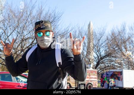 Washington DC, USA 11-29-2020: A young hispanic man wearing baseball hat, polarized designer sunglasses and face mask due to COVID-19 is posing with r Stock Photo