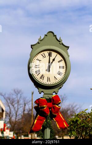 A red ribbon is tied as a Christmas holiday decoration on a green metal clock tower located at a shopping center. Clock tower has a vintage look with Stock Photo