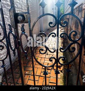 An abstract image of a narrow passageway behind locked gate. The stylish metal railings and the brick floor gives a mysterious look that is out of rea Stock Photo