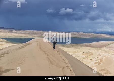 Tourist walking along the edge of the sand dune. Large barkhan in Mongolia sandy dune desert Mongol Els. Govi-Altay, Mongolia. Stock Photo
