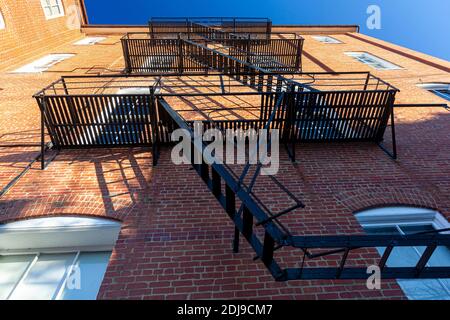 Bug eye view of vintage black metal construction fire escape ladder with makeshift balconies and access to egress windows attached on the side of an o Stock Photo