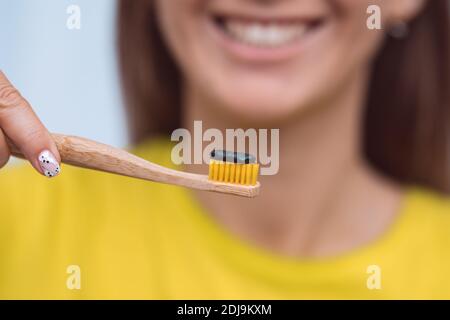 Close-up of smiling woman holding eco friendly bamboo toothbrush with black charcoal toothpaste near her mouth. Stock Photo